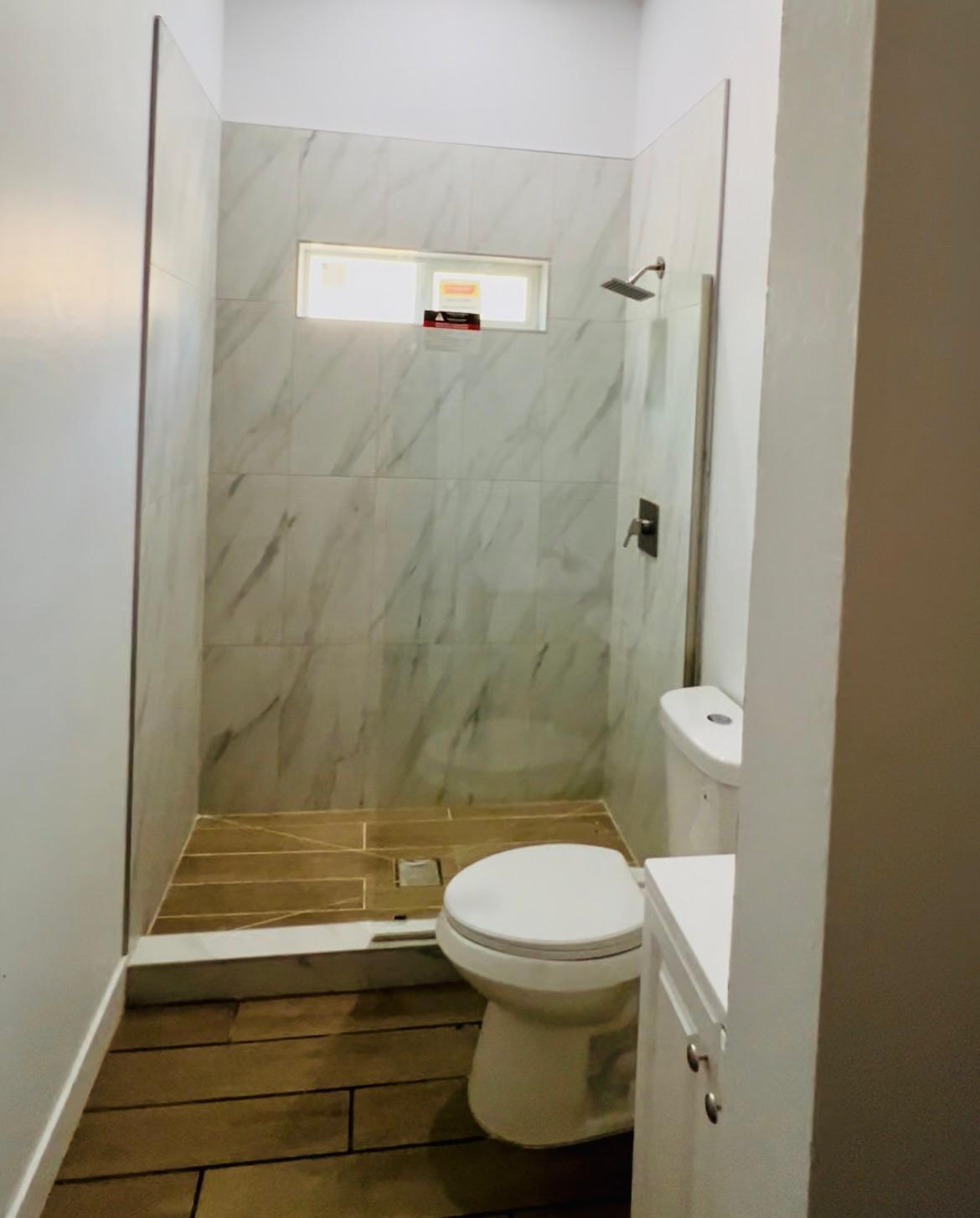 Baño con ducha de mármol, nicho con ventana y vanidad blanca