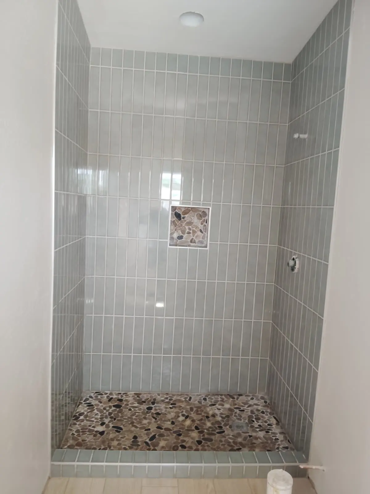 Baño interior con regadera, azulejo verde y piso de piedra de río