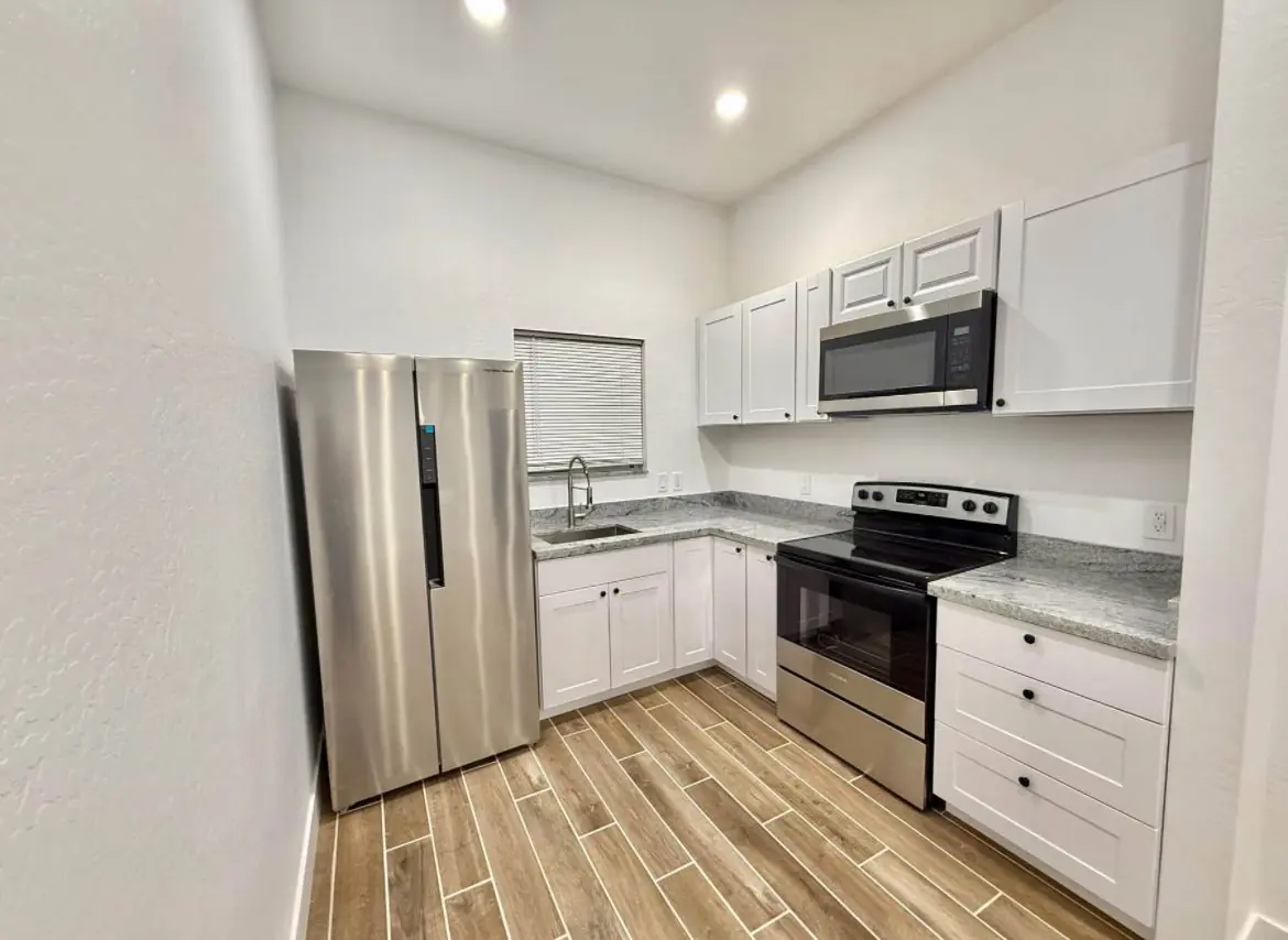 Cocina terminada con vista amplia, gabinetes blancos y piso tipo madera